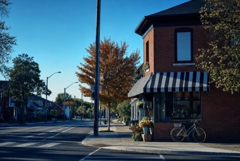 A red-brick corner shop with a striped awning, flowers and a bicycle outside on a clear autumn day